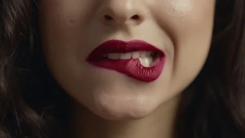 Sensual girl biting sexy plump lips. Close up view of young female face.